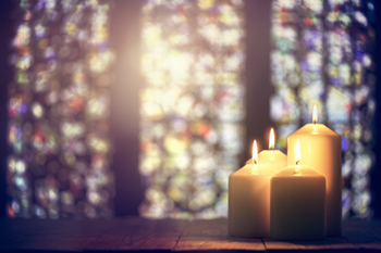 Four lit Advent candles in a window beside stained glass